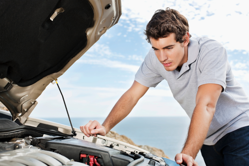Young man looks under the hood of his car for engine trouble. Horizontal shot.